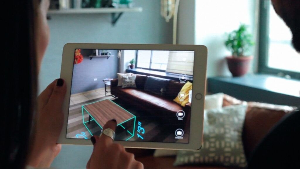(Sube una imagen de una persona usando una tablet o smartphone con AR para visualizar muebles en su hogar, con un agente virtual amigable en la pantalla. Tamaño: 1200x630 píxeles. Añade el texto ALT: "Muebles AR Agente Virtual")